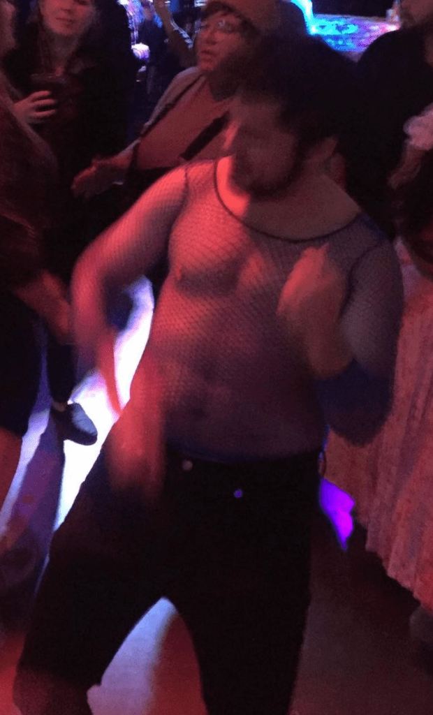 Candid image of James dancing and wearing a blue, long sleeve mesh shirt and skinny jeans. 